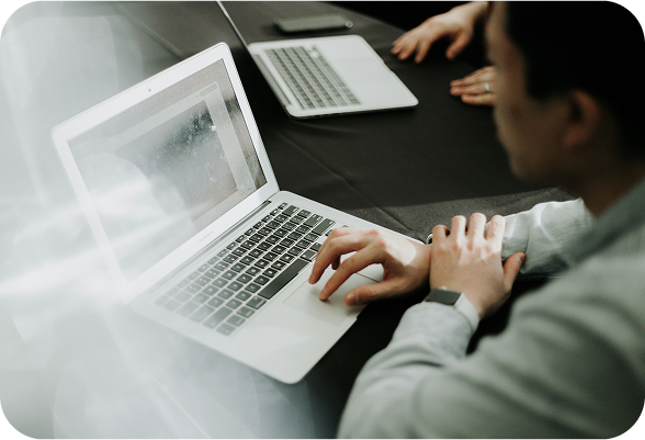 Individual working on a laptop at a table, appearing engaged and concentrated.